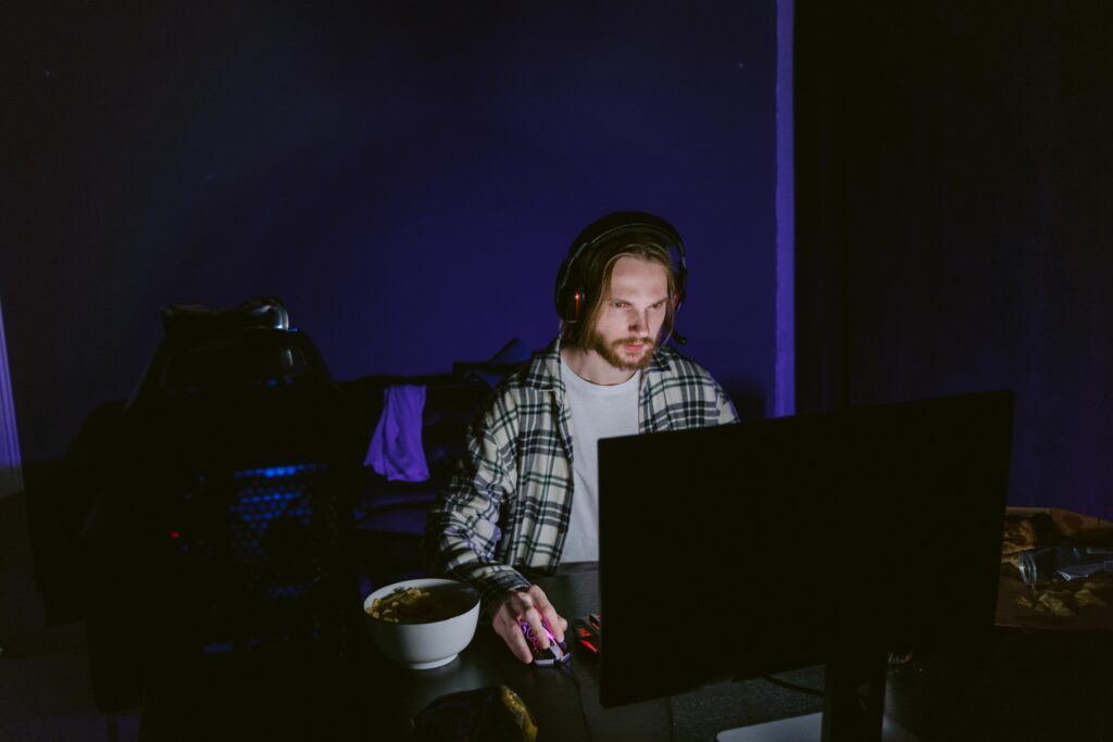 A focused man playing video games on a computer at night with a headset.