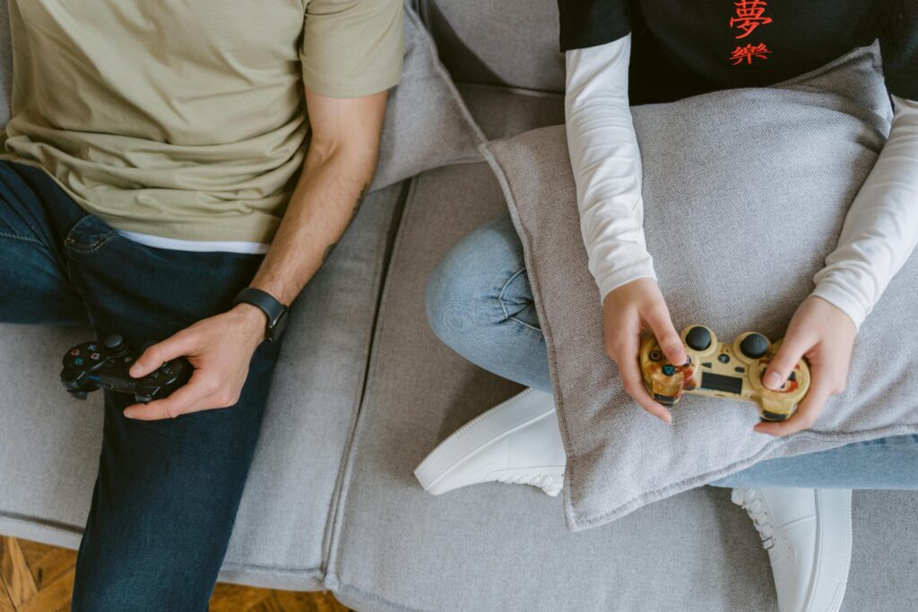 A close-up of two individuals enjoying video games with controllers on a sofa.