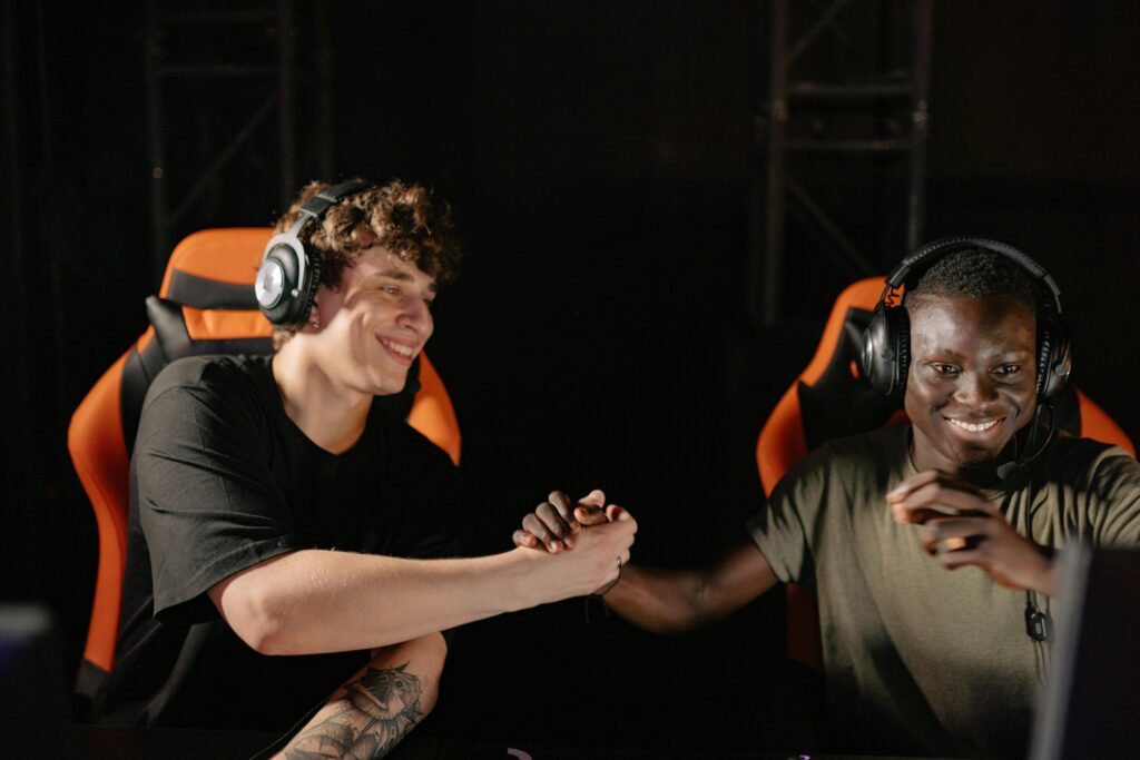 Two young gamers shaking hands and celebrating a win together indoors.